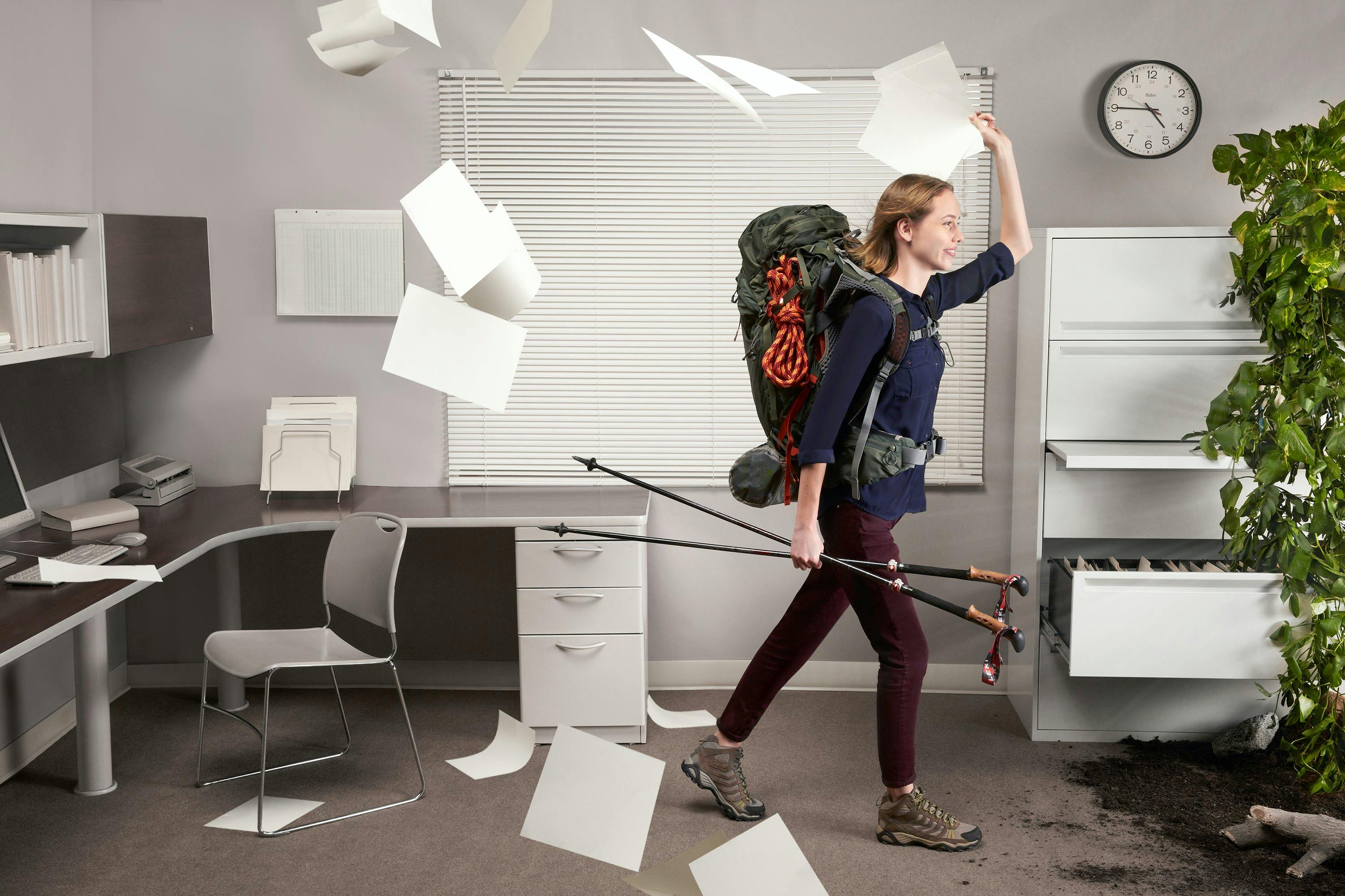 woman with hiking gear throwing papers in the air walking out of the office 