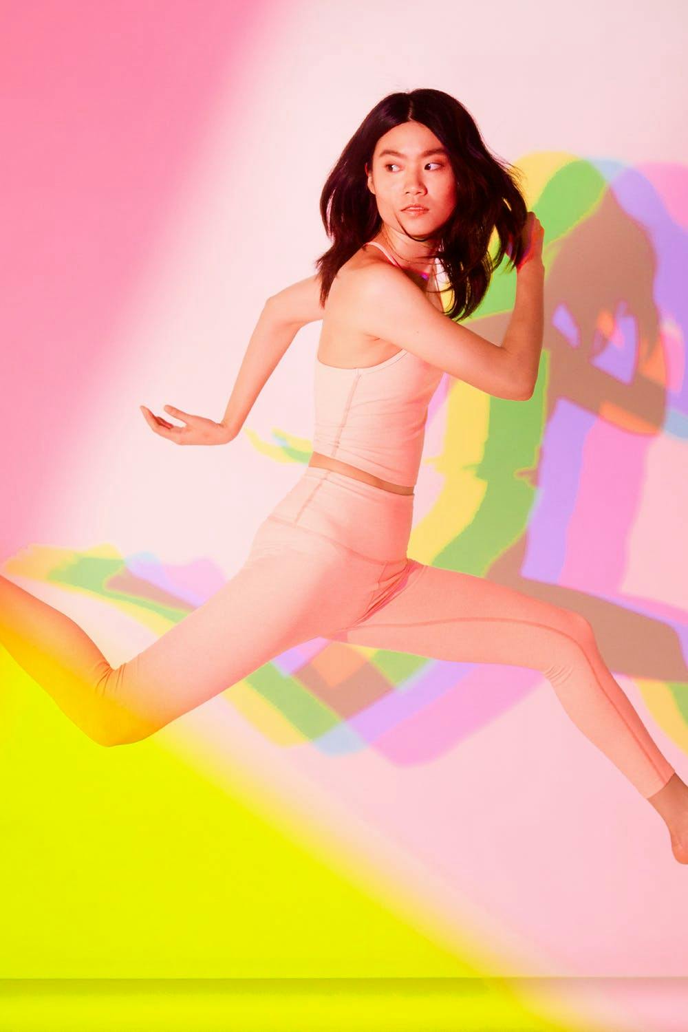 model photography of a model in an action shot jumping across the shot in pink beyond yoga clothes and colored filter lighting 