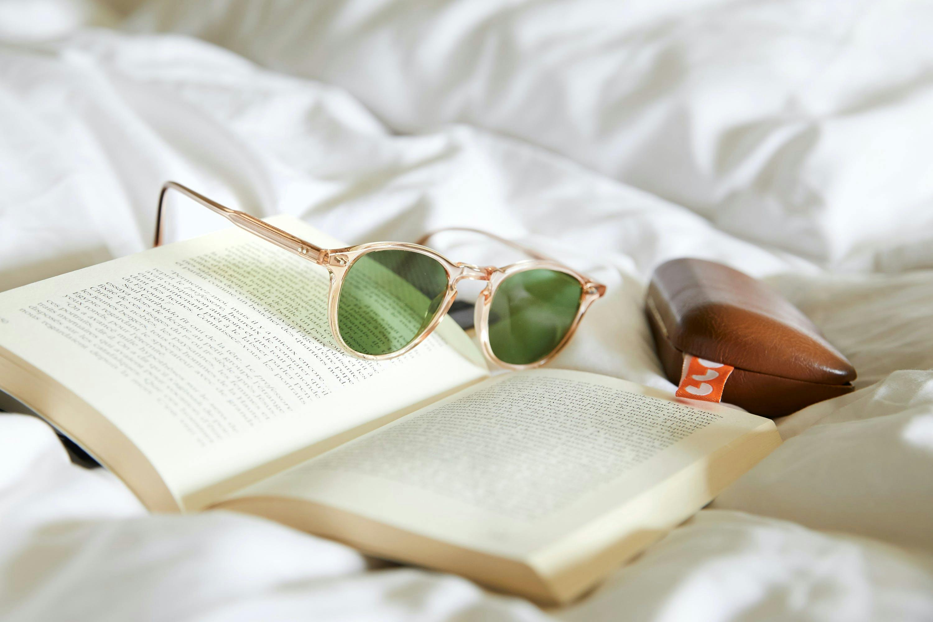 staged sunglasses, book, on bed, cream color palette with natural light product photography 