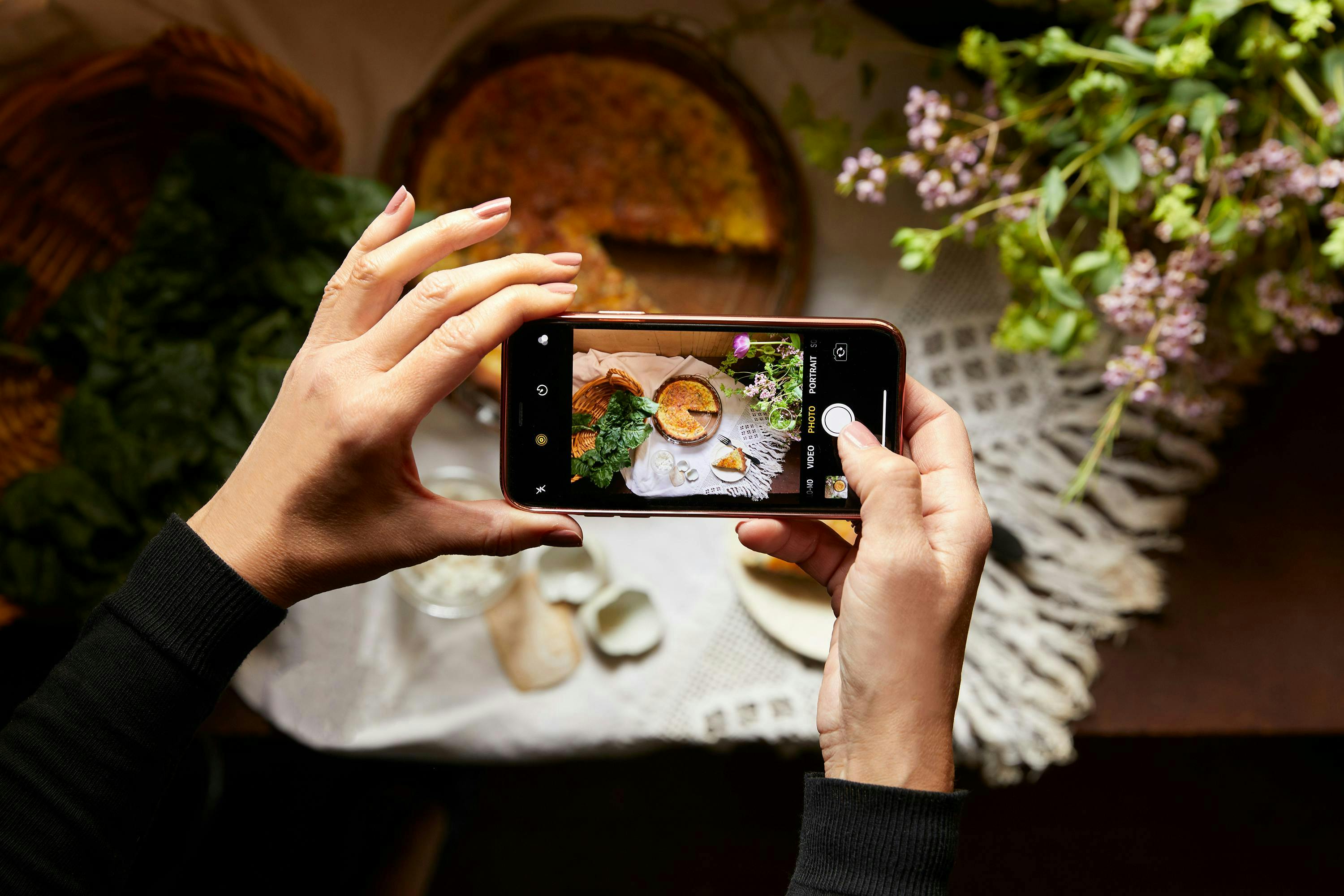 Photograph of an iPhone held up to take a picture of a freshly baked pie with a golden crust and steam rising from the top.
