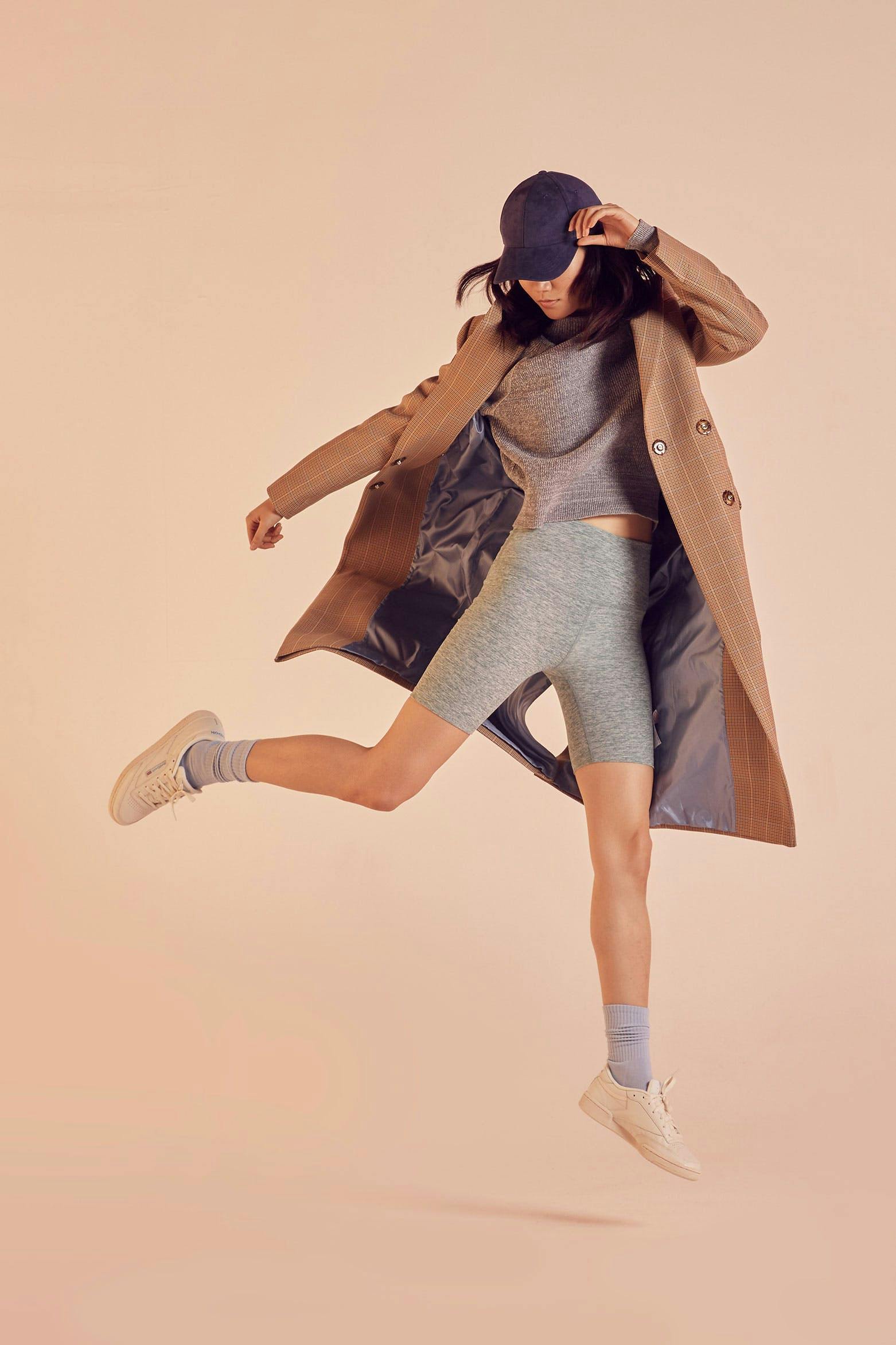 fashion model photography with a model in an action jump wearing bike shorts and a beige trench coat 